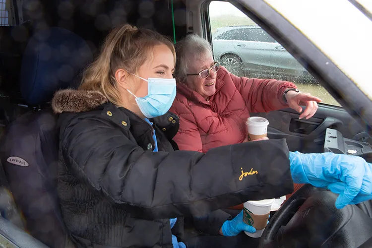 Care worker and woman smiling in a car drinking coffee